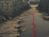 A drained castle moat with crumbling stone walls and a single ribbon of crimson red liquid running through the dry channel.